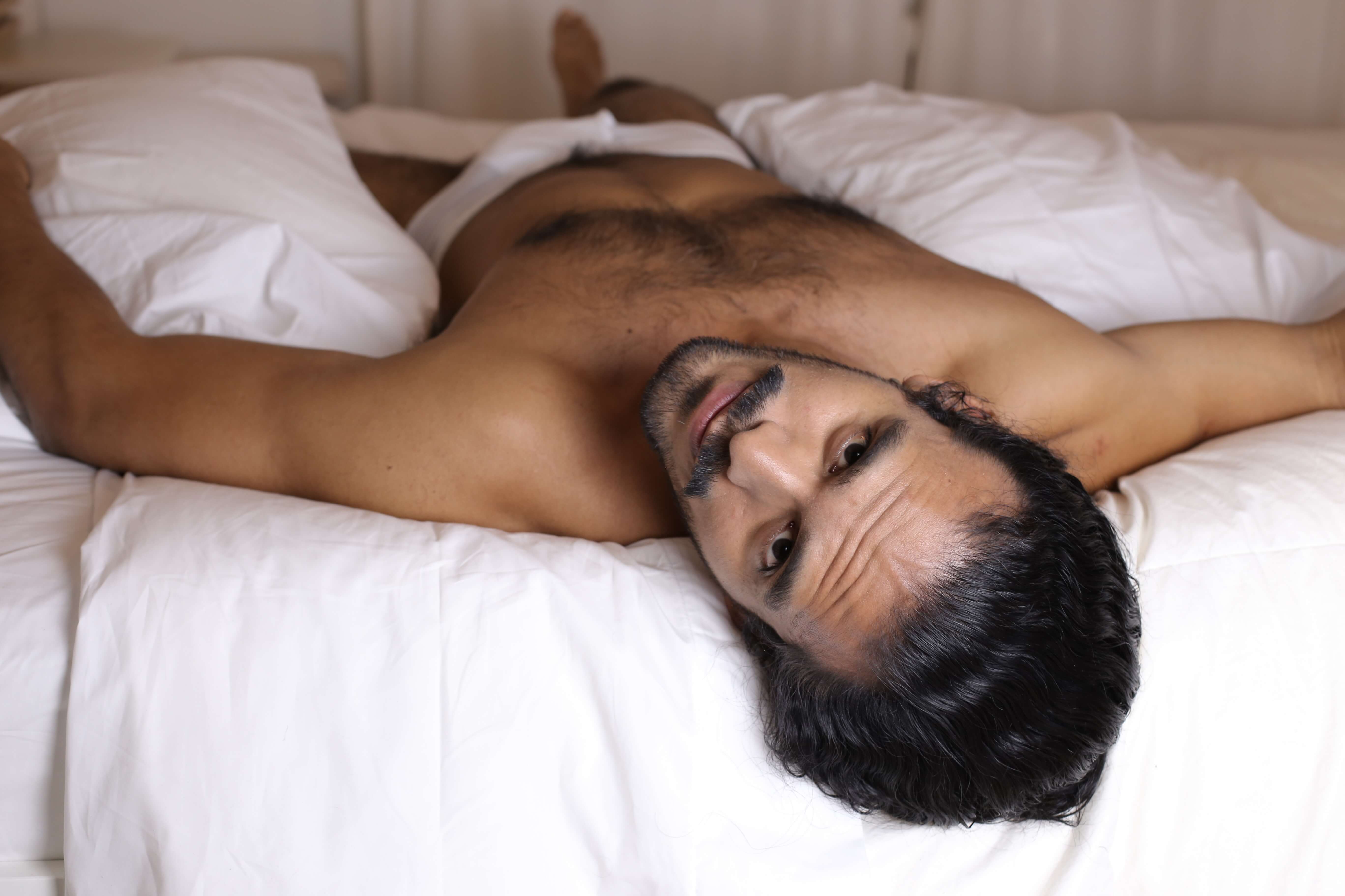 A young shirtless man lying in bed